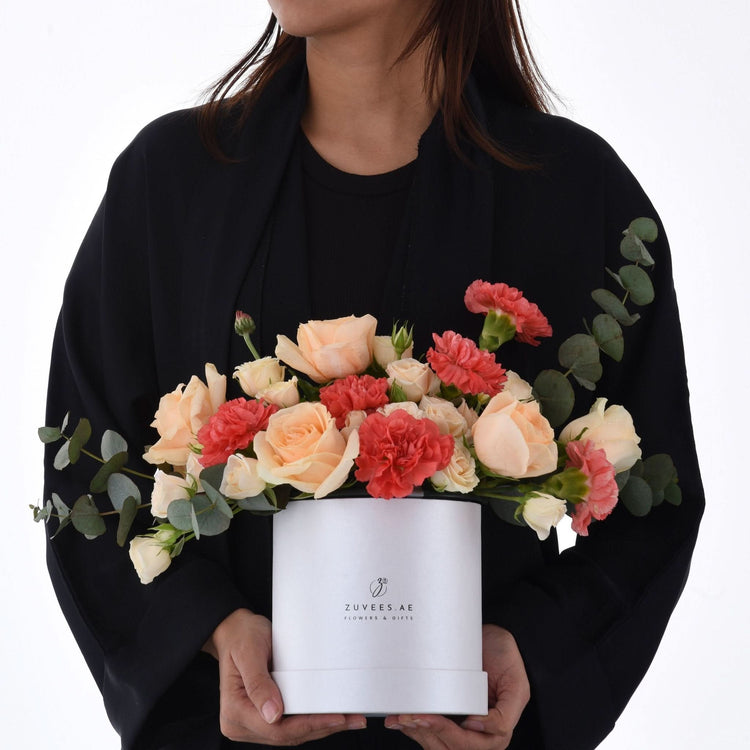 White box holds peach roses and coral carnations with eucalyptus.