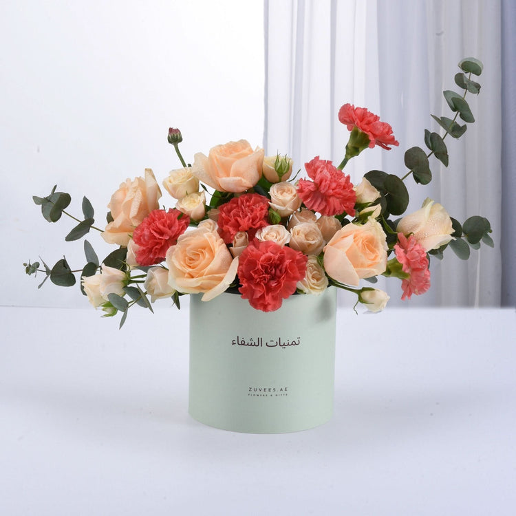 Pastel peach roses and coral carnations in mint-green cylindrical vase.