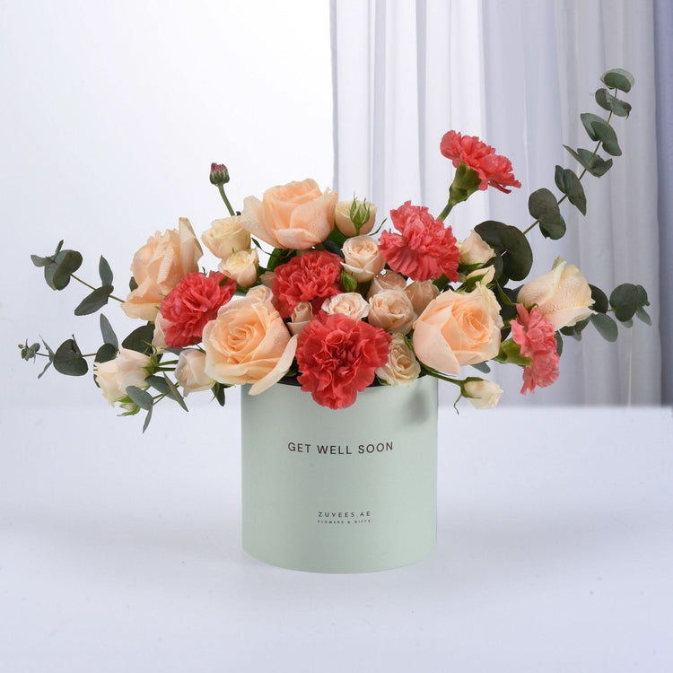 Pastel mint box holds peach roses and coral carnations with eucalyptus.