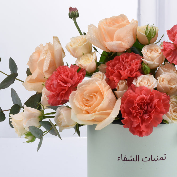 Soft peach roses and coral carnations glisten with dewdrops in mint vase.