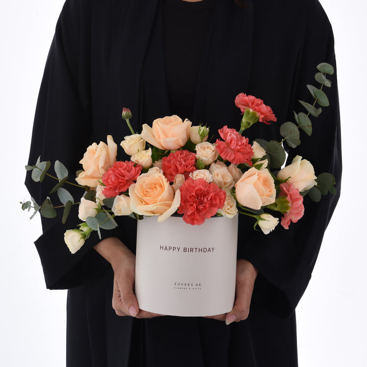 Elegant peach roses, coral carnations, and eucalyptus in a "Happy Birthday" gift box.