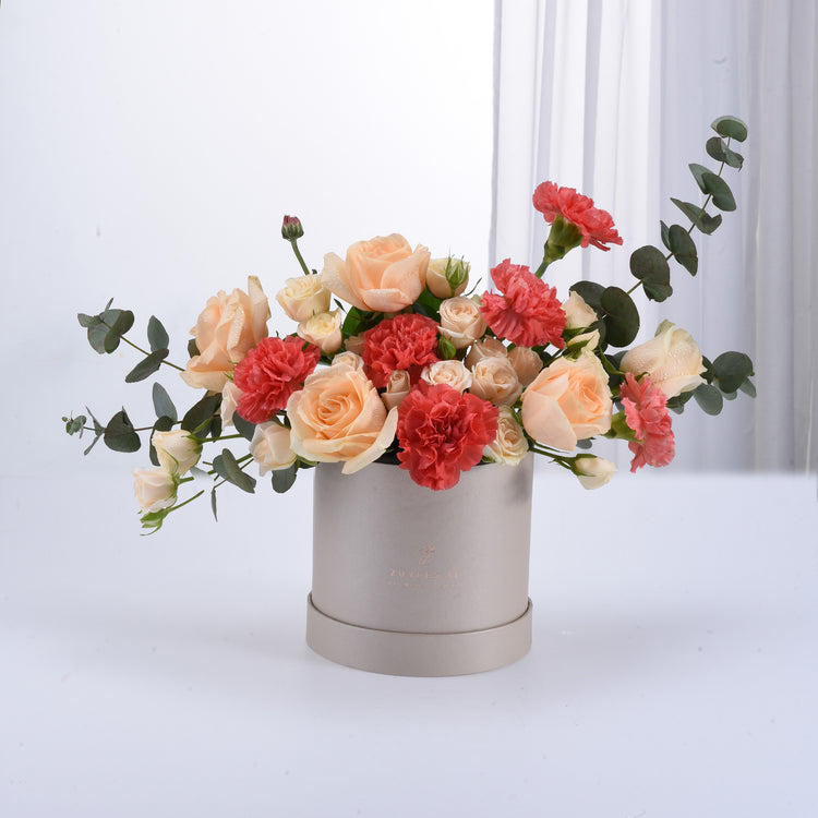 Soft peach roses and coral carnations in sleek silver box.