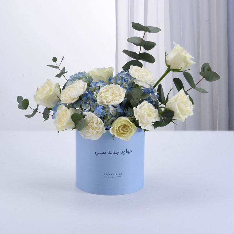 Light blue box holds white roses and blue hydrangeas with eucalyptus.
