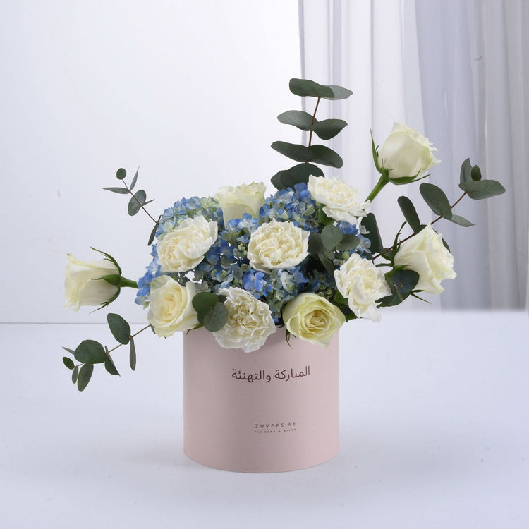 Elegant white roses, blue hydrangeas, eucalyptus in blush pink gift box with Arabic text.