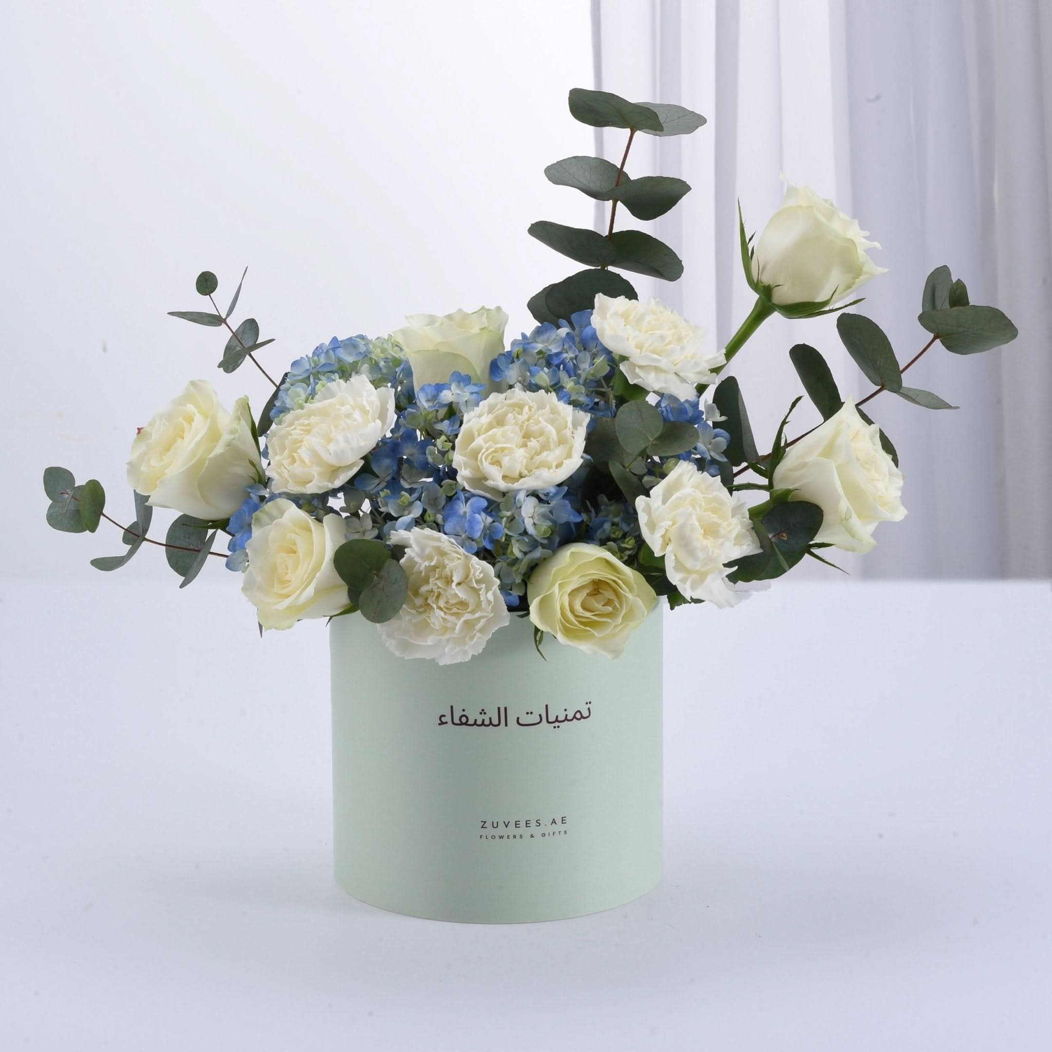 Soft mint box holds creamy white roses, blue hydrangeas, and eucalyptus.