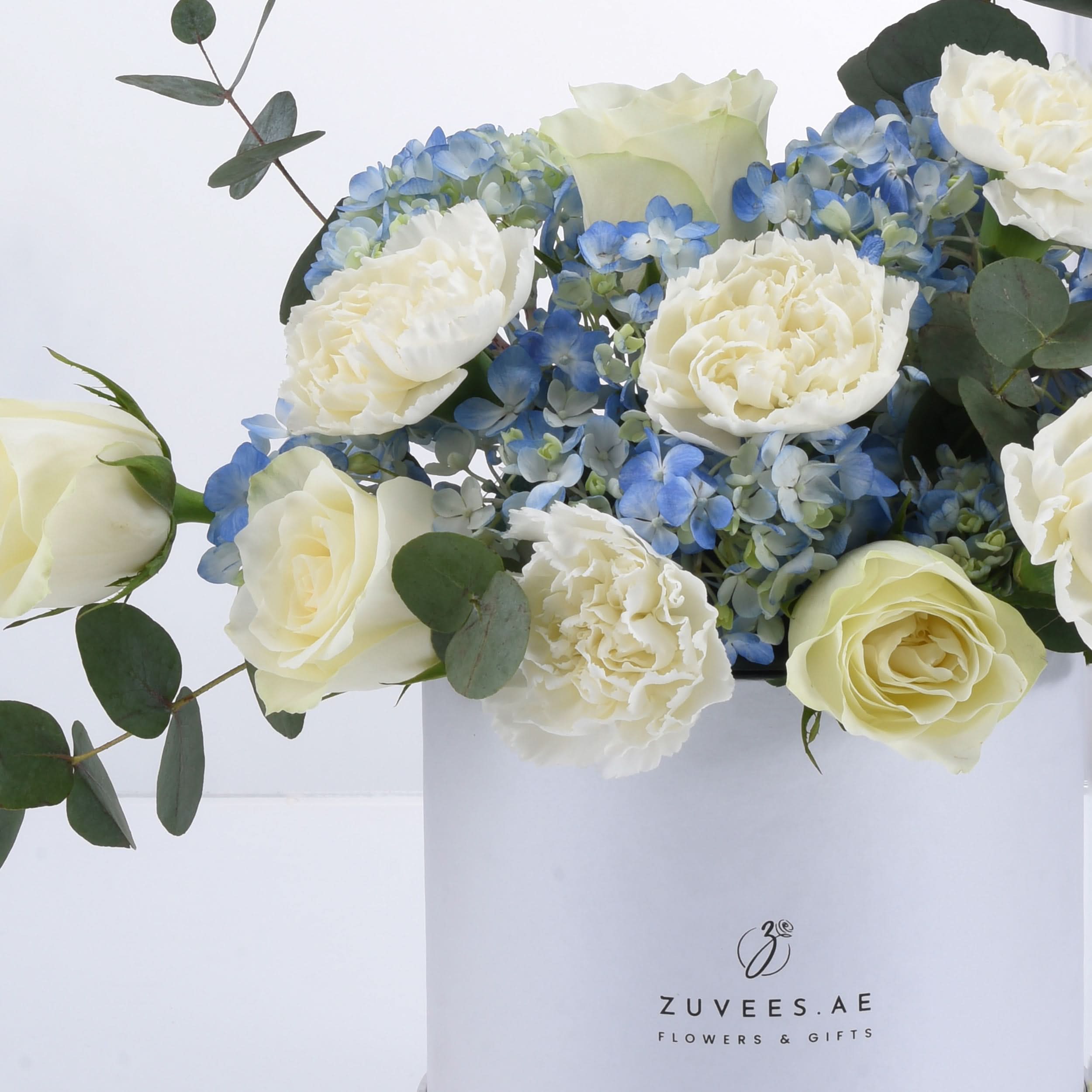 Elegant white roses, peonies, and blue hydrangeas in minimalist white box.