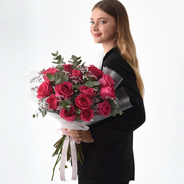 Vibrant pink roses, eucalyptus, baby’s breath bouquet wrapped in white, held by woman in black.