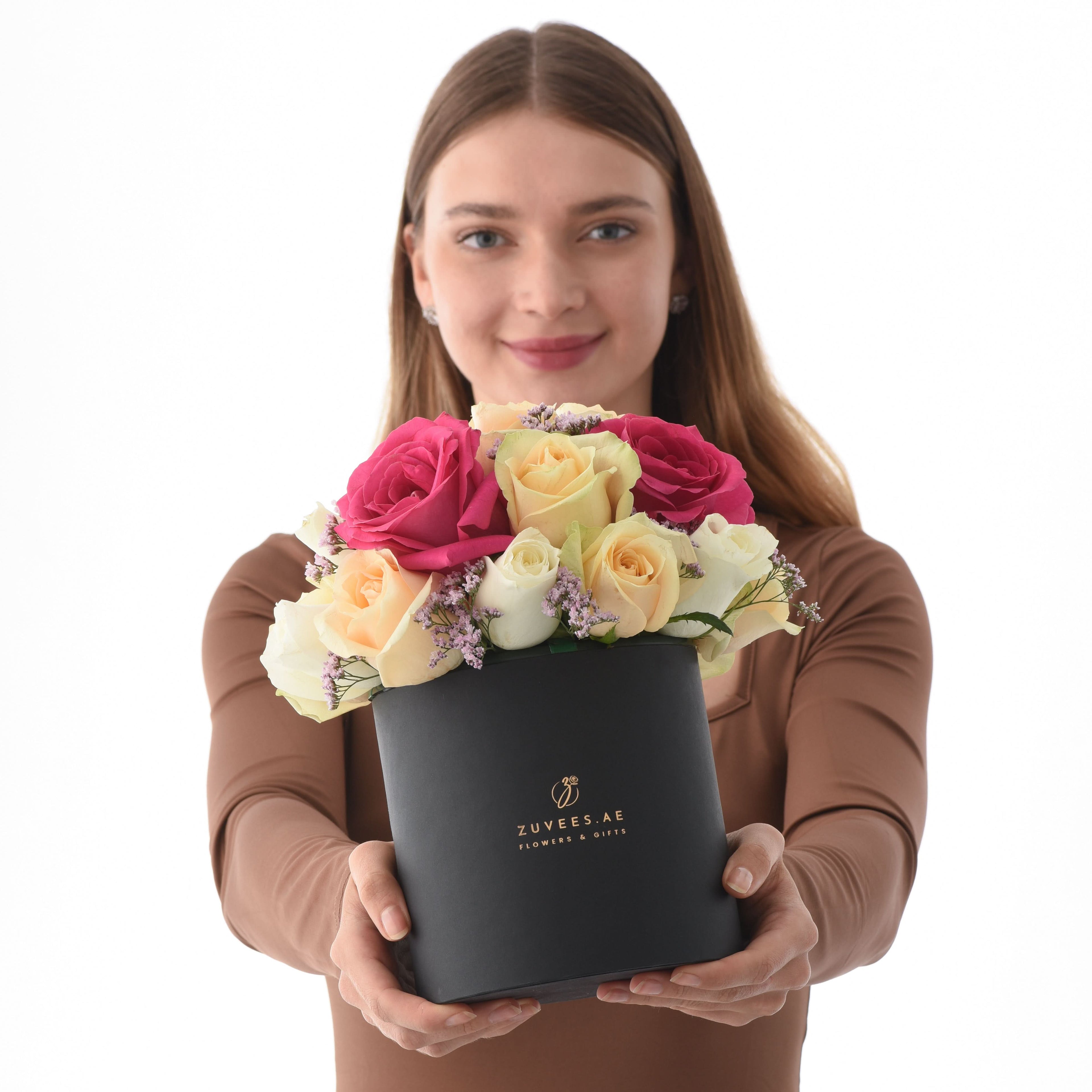 Woman holds elegant black box of vibrant pink, yellow, and white roses with lavender accents.