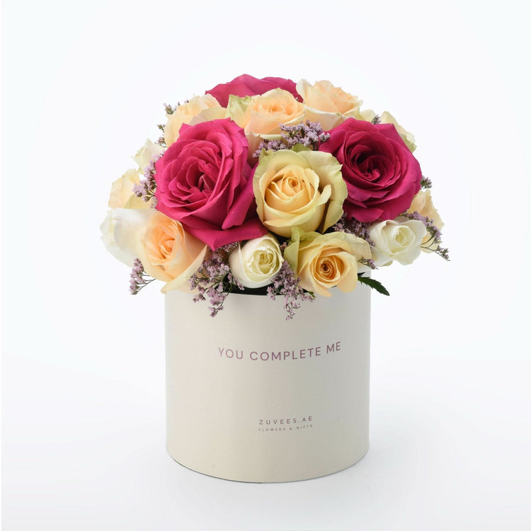 Cream box holds vibrant pink, yellow, and white roses with purple filler blooms.