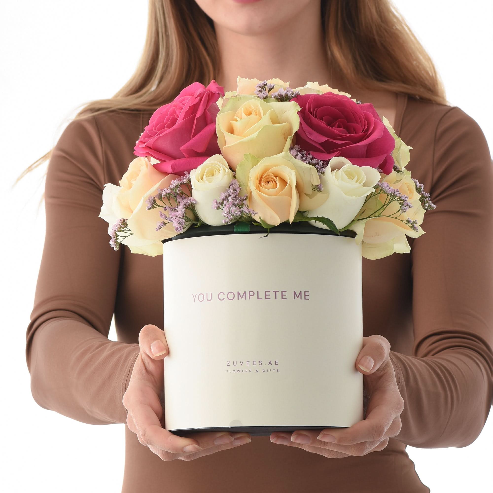 Vibrant pink, cream, yellow roses in elegant white "You Complete Me" gift box, held gently.