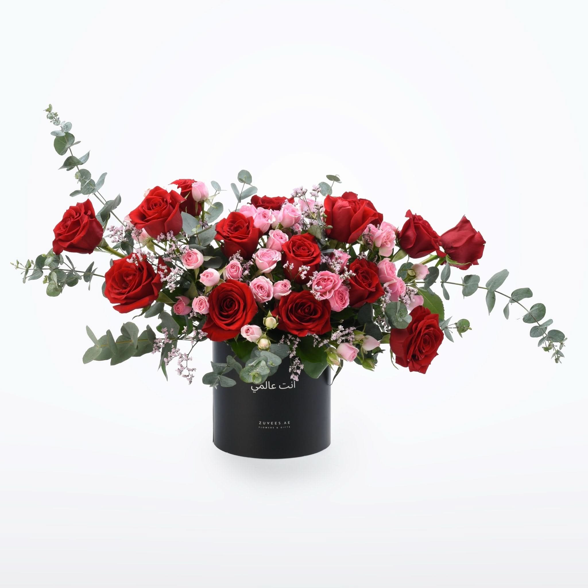Vibrant red and pink roses with eucalyptus in sleek black cylindrical vase.