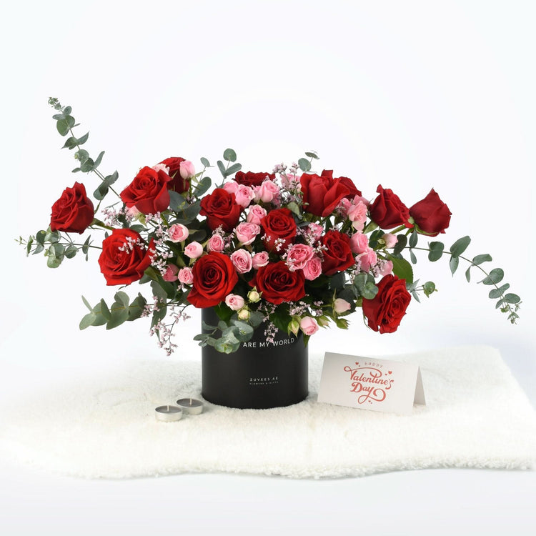 Vibrant red and pink roses in black cylindrical vase with Valentine’s card and candles.