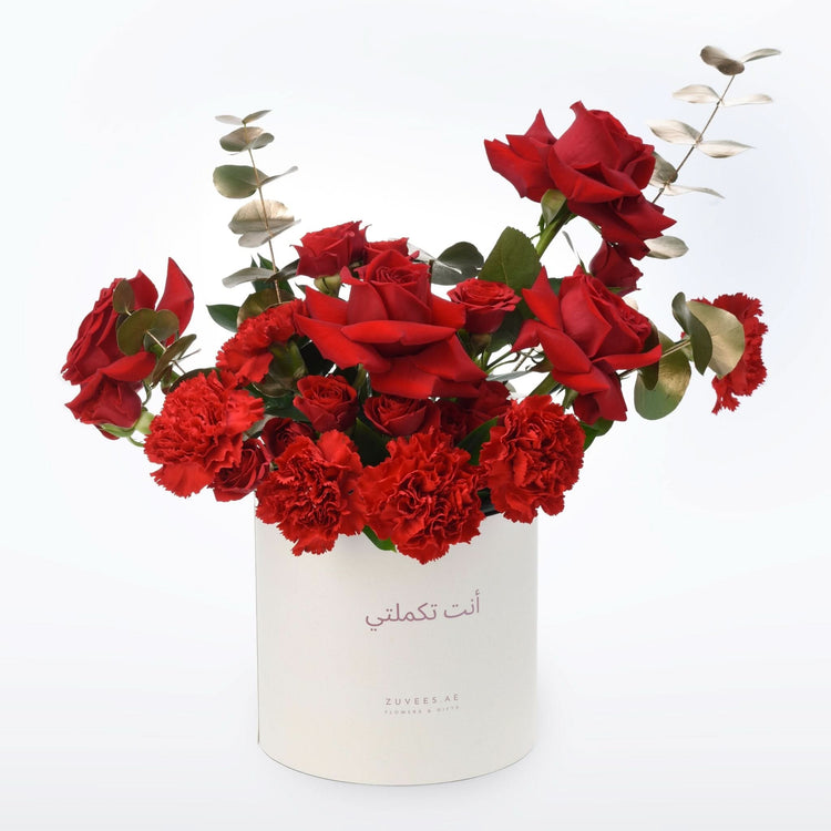 Vibrant red roses and carnations in white cylindrical box with Arabic script.