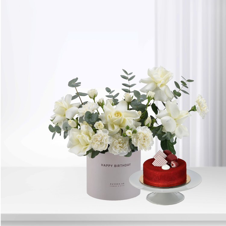 White roses & eucalyptus in "Happy Birthday" box beside red velvet cake, elegant gift set.