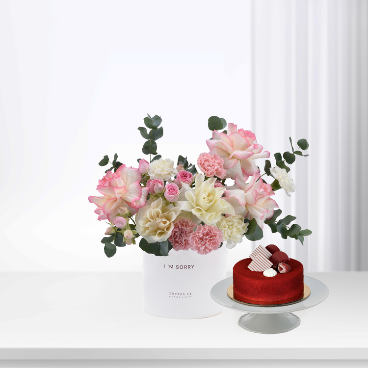 Soft pink and white roses with eucalyptus, beside red velvet cake on stand.