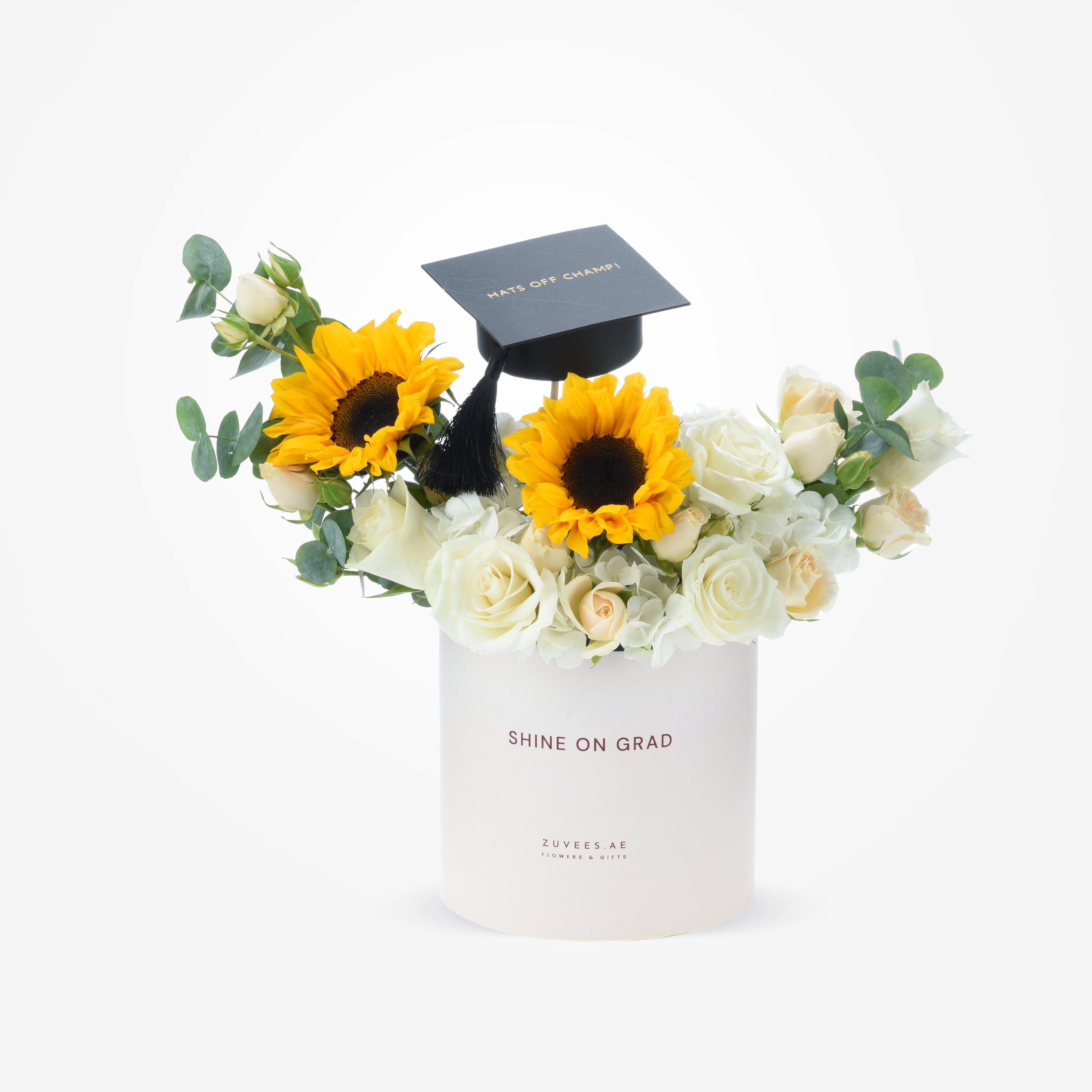 White cylinder holds vibrant sunflowers and roses, topped with graduation cap.