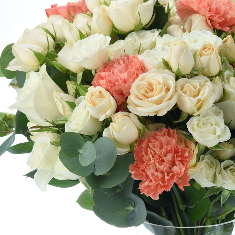 Cream roses, coral carnations, and eucalyptus in a lush, elegant bouquet arrangement.
