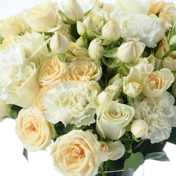 Creamy white roses and carnations with green leaves in elegant bouquet arrangement.