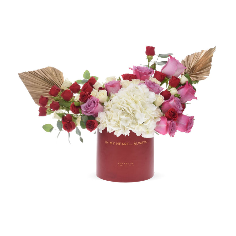 Vibrant red, pink, and white roses with hydrangeas and gold fans in a red box reading "IN MY HEART... ALWAYS".
