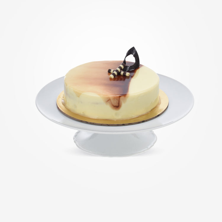 Glossy caramel-topped cake with chocolate swirl, striped sticks, on white pedestal stand.