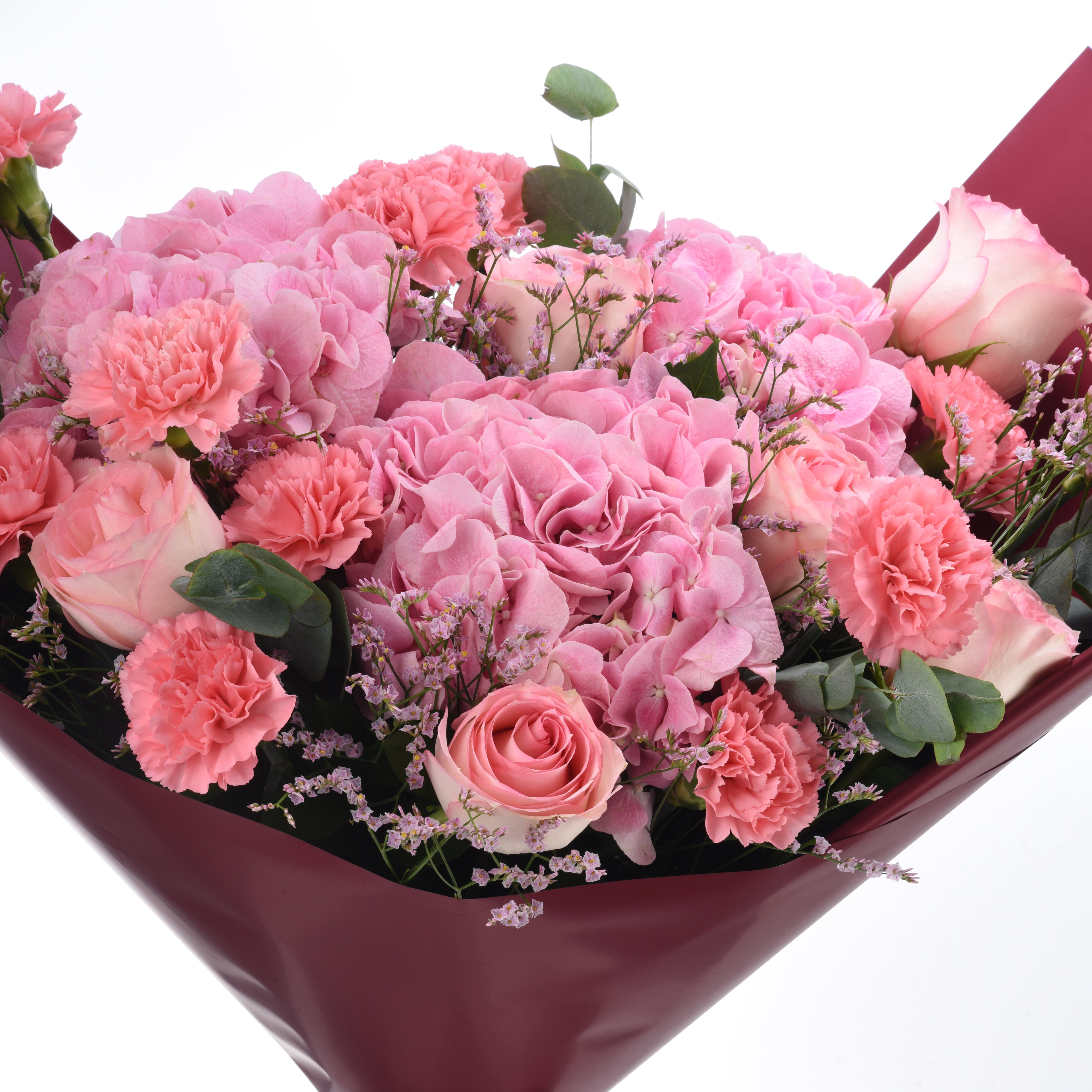 Pink roses, carnations, and hydrangeas wrapped in burgundy paper.