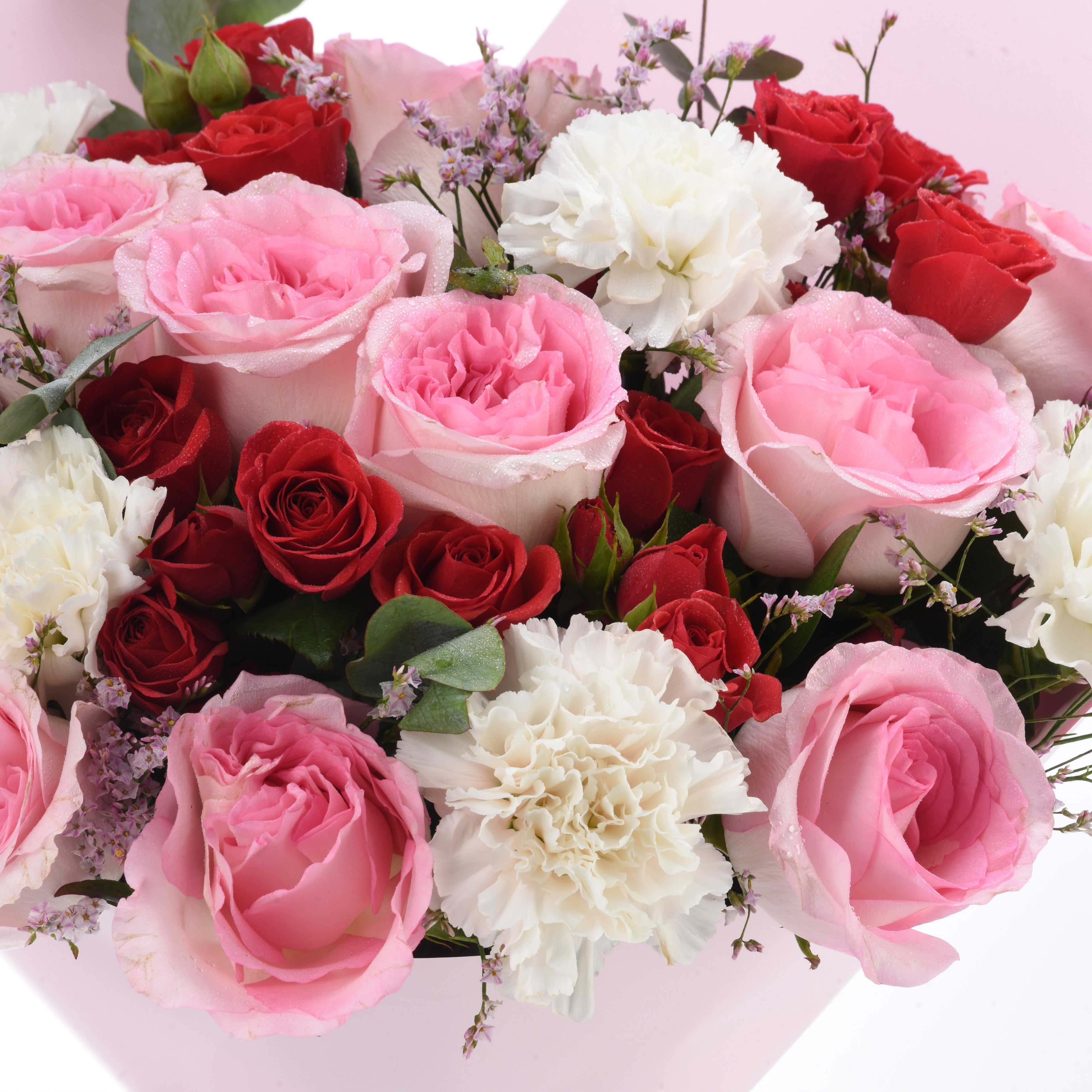 Vibrant pink, red, and white roses with delicate carnations and dewdrops, set against soft pink background.