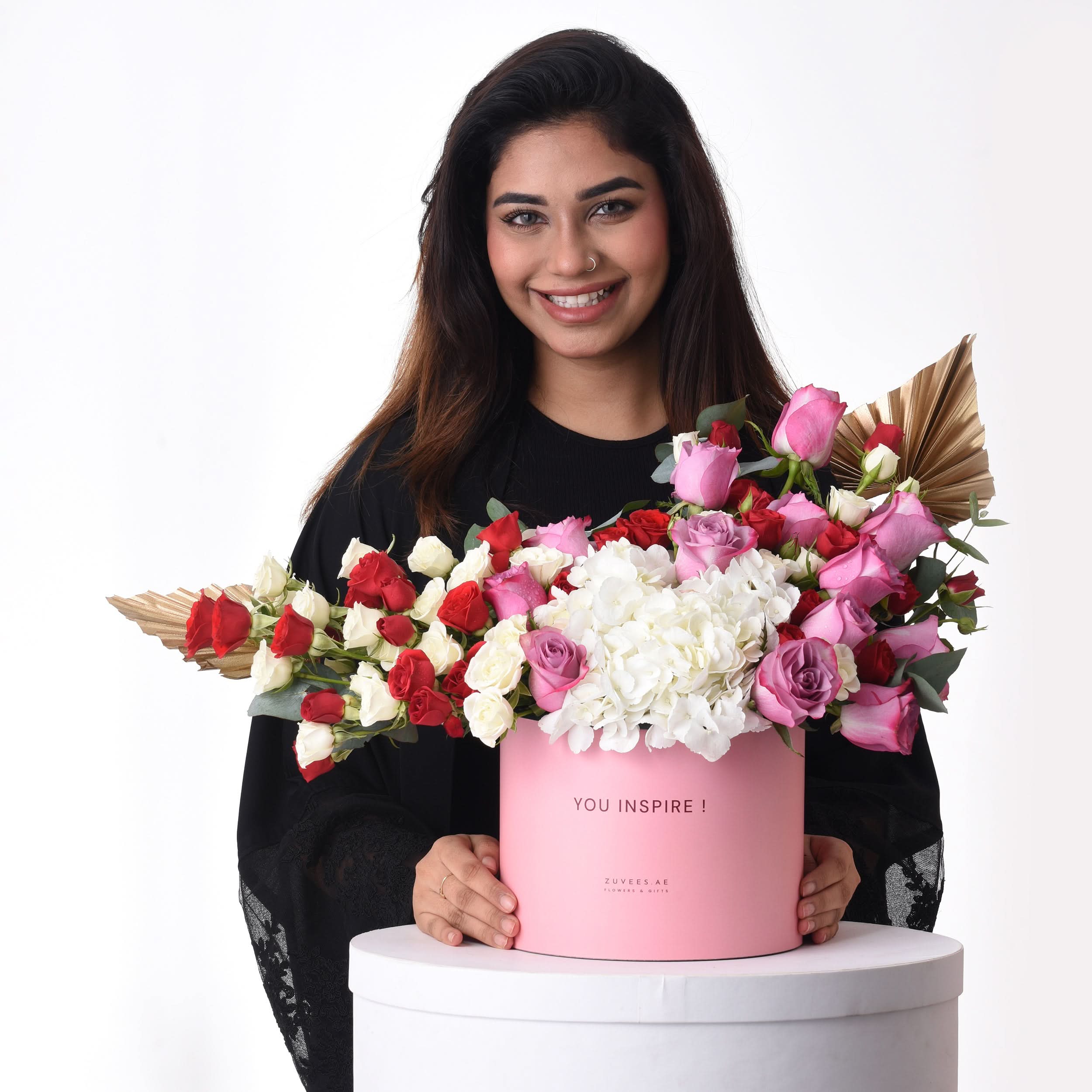 Pink box holds vibrant red, white, and pink roses with gold accents.