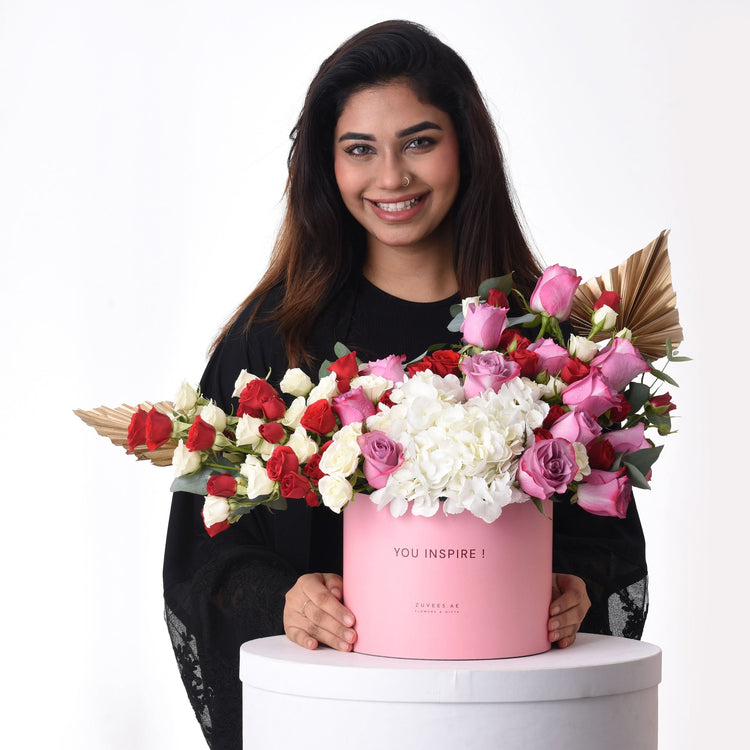 Pink box holds vibrant red, white, and pink roses with gold accents.