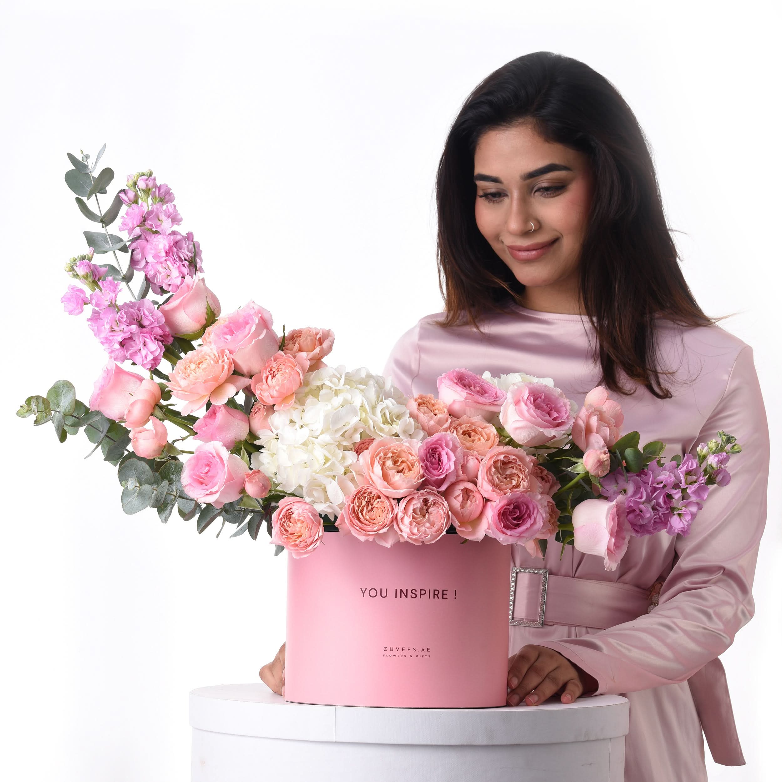 Pink floral arrangement in branded box, woman smiles, soft pastel tones.