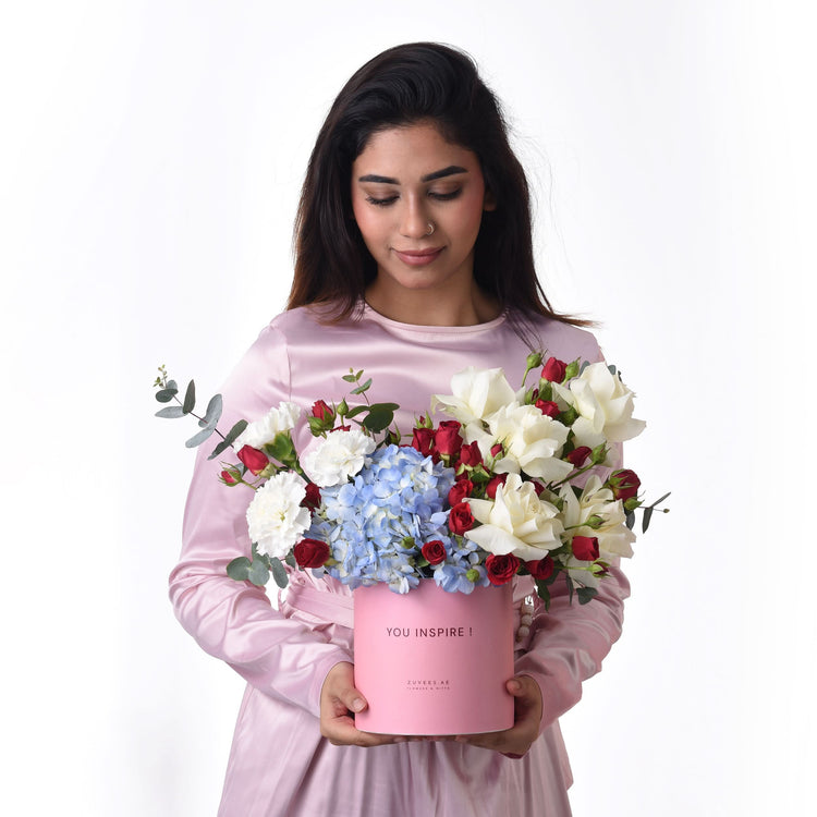 Pink box holds red, white roses and blue hydrangeas, with "YOU INSPIRE!" message.