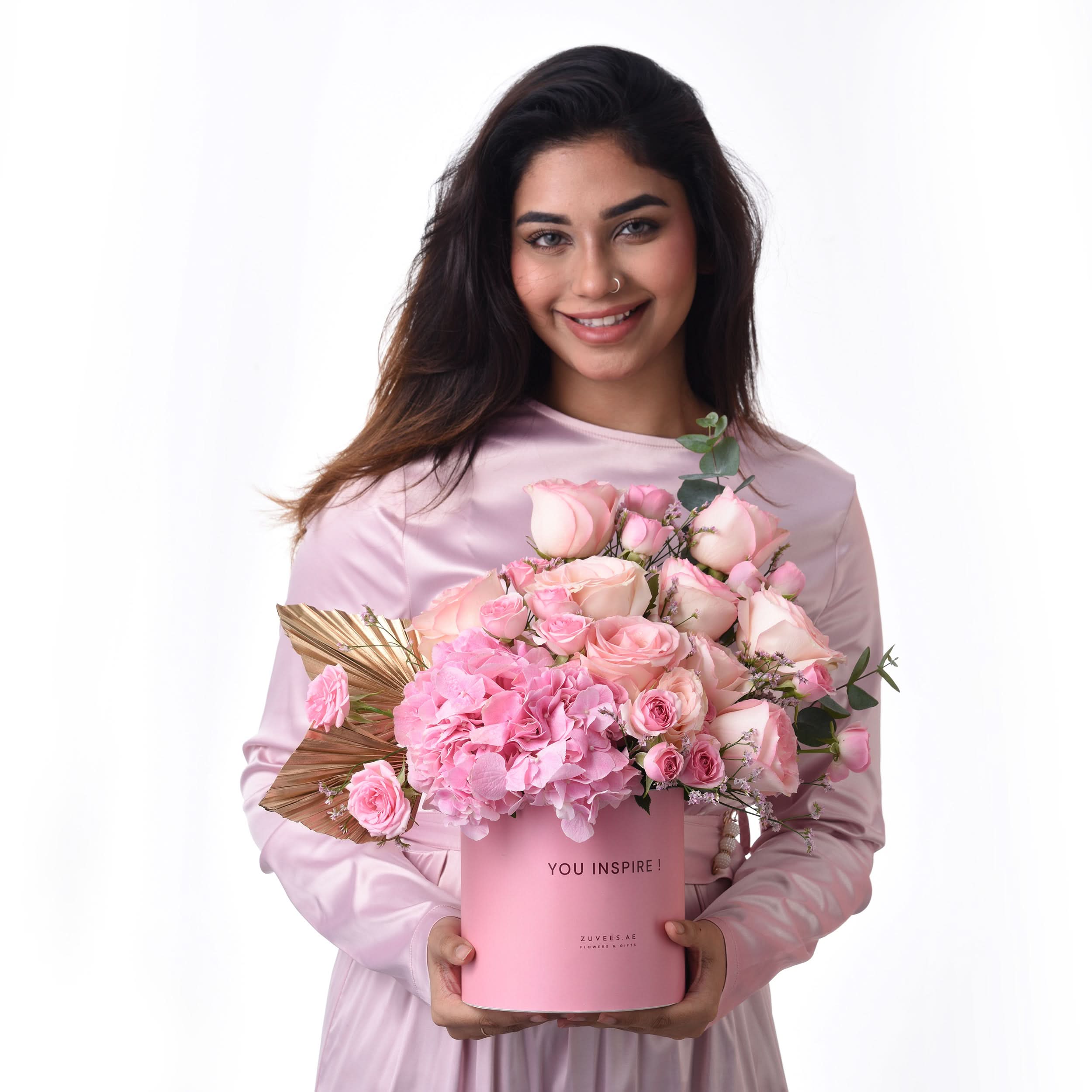Pink rose and hydrangea bouquet in branded box, held by smiling woman.