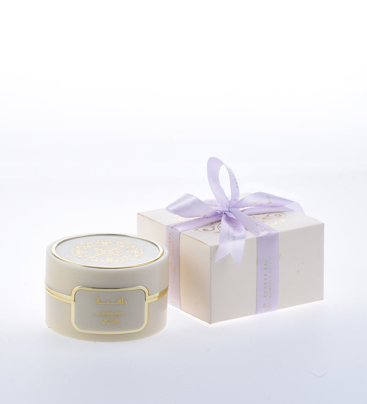 Cream jar with gold trim and Arabic label, beside lavender-bowed gift box.