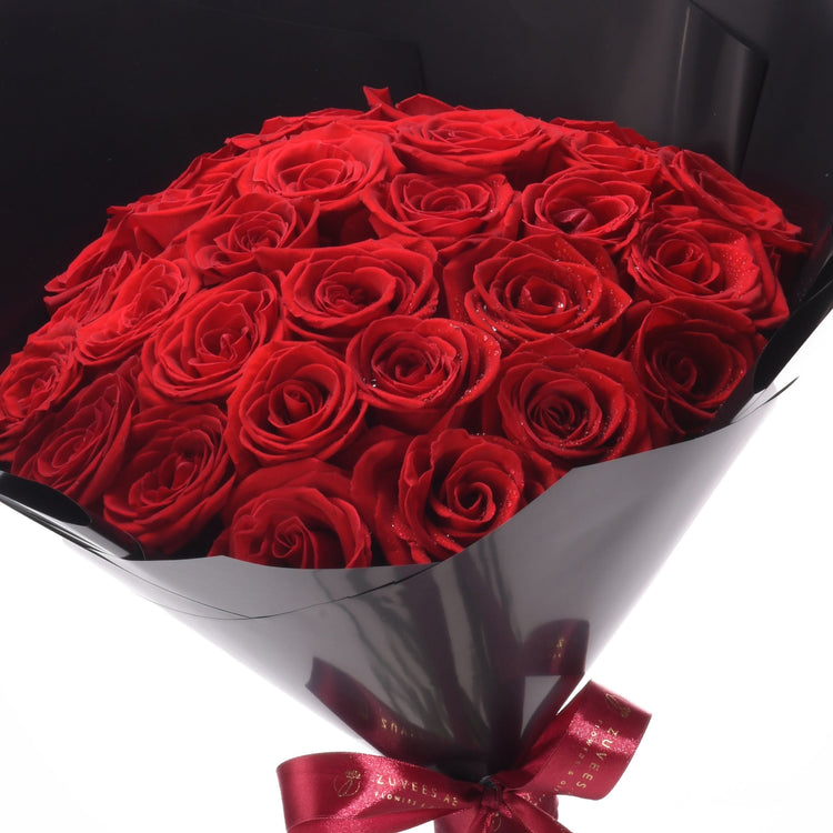 Vibrant red roses in glossy black wrap, accented with a red satin bow.