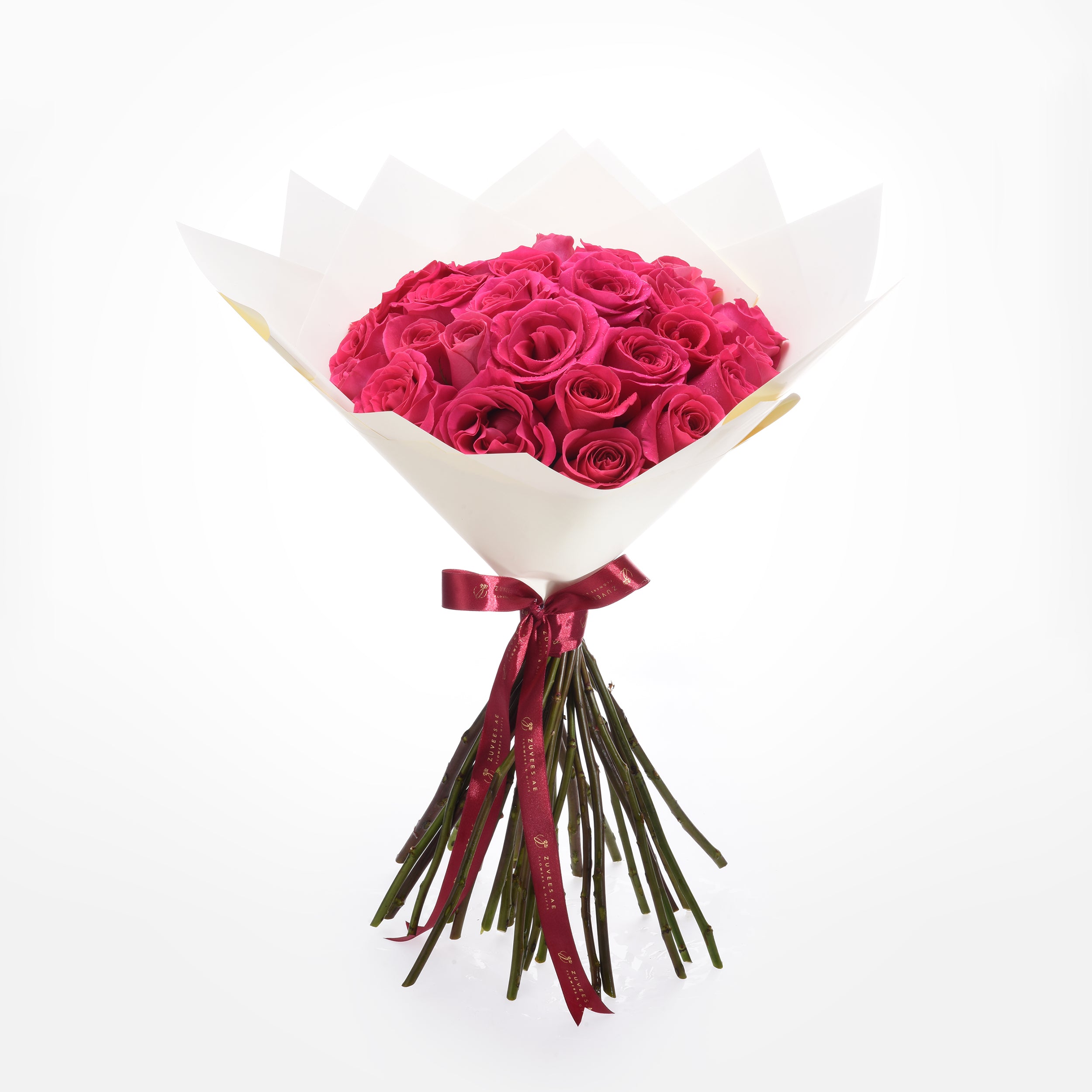 Vibrant fuchsia roses in white paper, tied with burgundy ribbon.