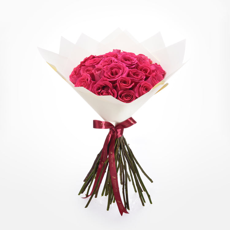 Vibrant fuchsia roses in white paper, tied with burgundy ribbon.