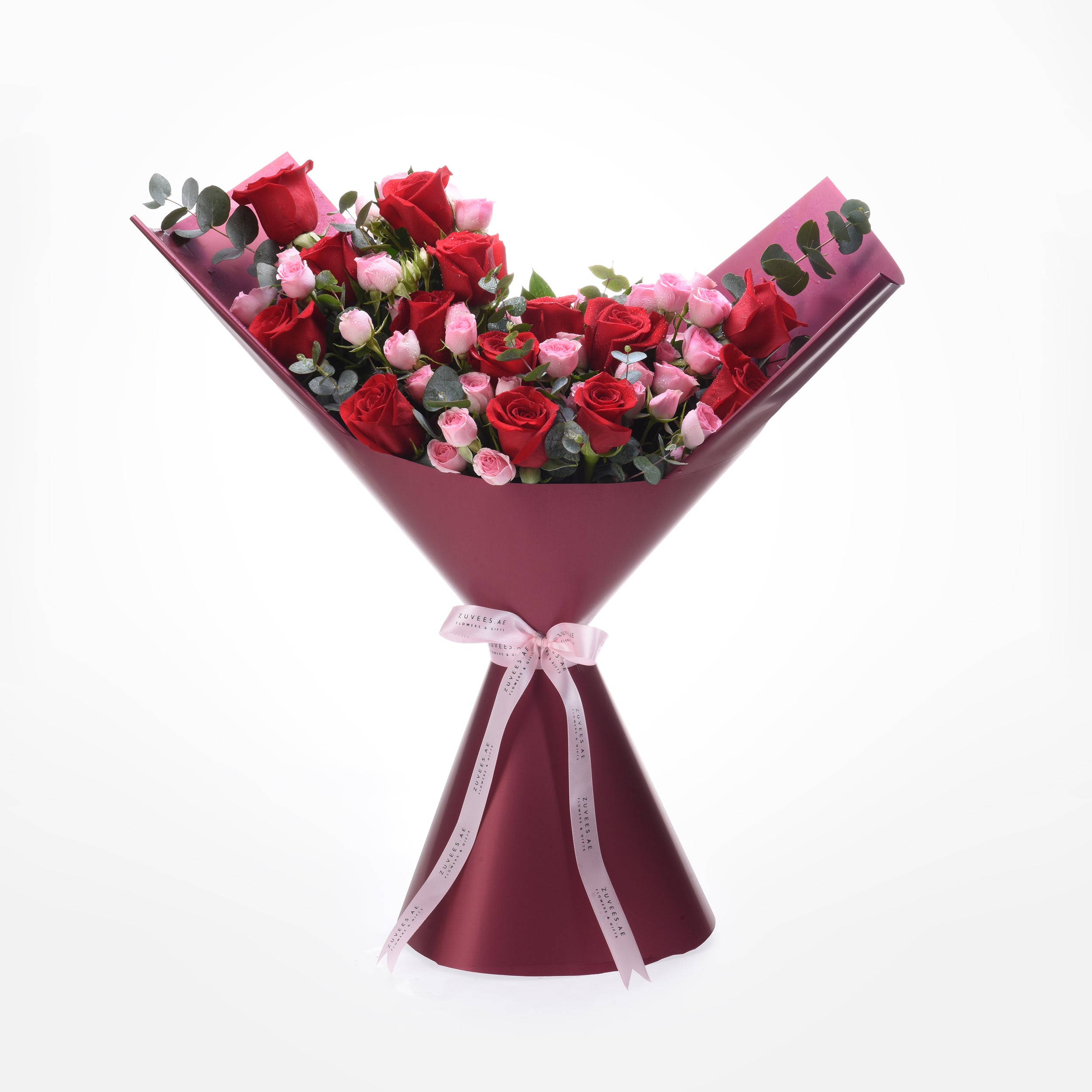 Vibrant red and pink roses wrapped in burgundy paper with elegant pink ribbon bow.