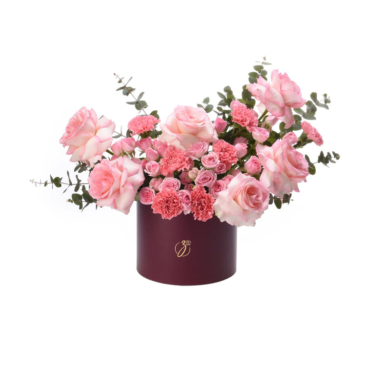 Elegant pink roses and carnations in burgundy hat box with gold logo.