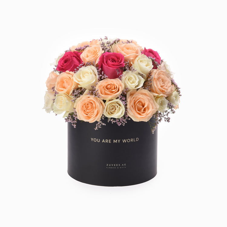 Black box holds vibrant peach, pink, and cream roses with lavender accents.