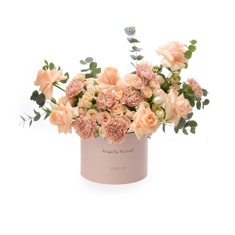 Soft peach roses and carnations in a branded pink box with Arabic greeting.