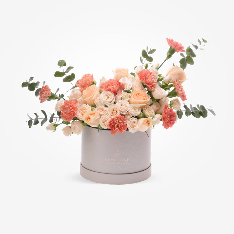 Soft peach roses and carnations in elegant silver hat box.