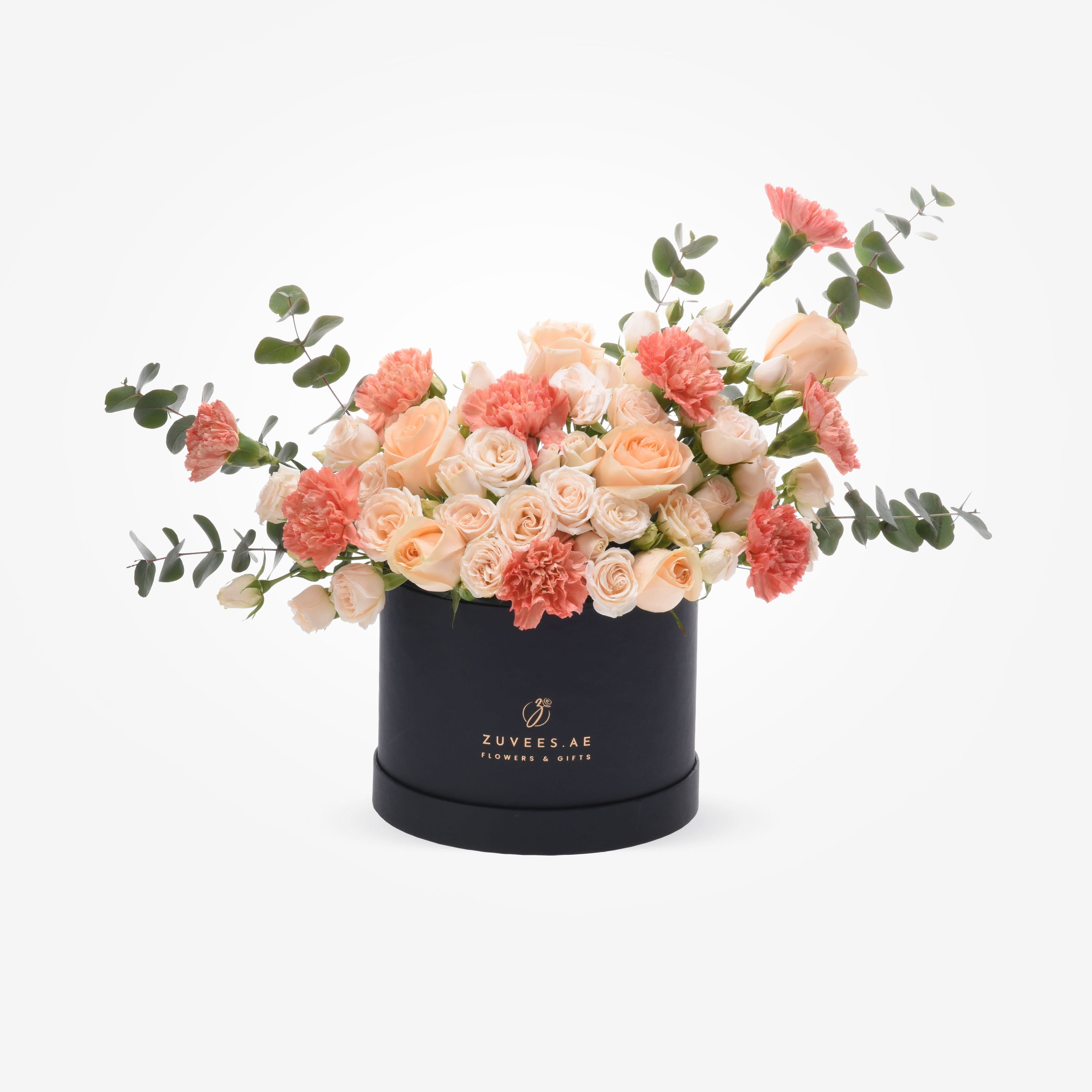 Elegant peach roses and coral carnations in a sleek black Zuvees box, accented with eucalyptus.