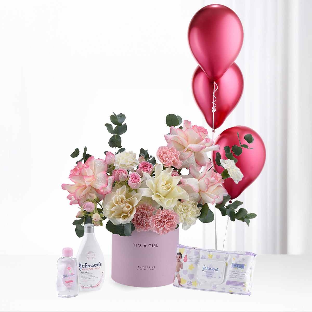 Pink floral arrangement with balloons, baby essentials, and "It&