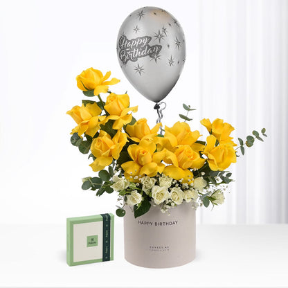 Vibrant yellow roses with white accents, silver "Happy Birthday" balloon, and branded gift box.