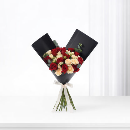 Elegant black-wrapped bouquet with red and cream roses, accented by eucalyptus and a white ribbon.