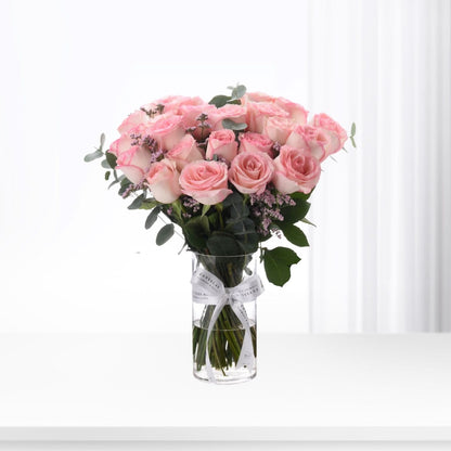Soft pink roses in clear vase, accented with greenery and lavender, tied with white ribbon.