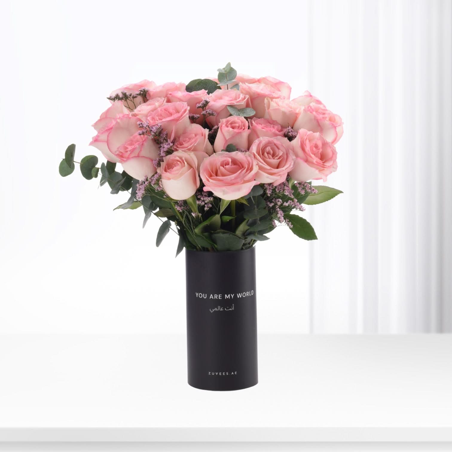Pink roses in black vase with bilingual message, minimalist white background.