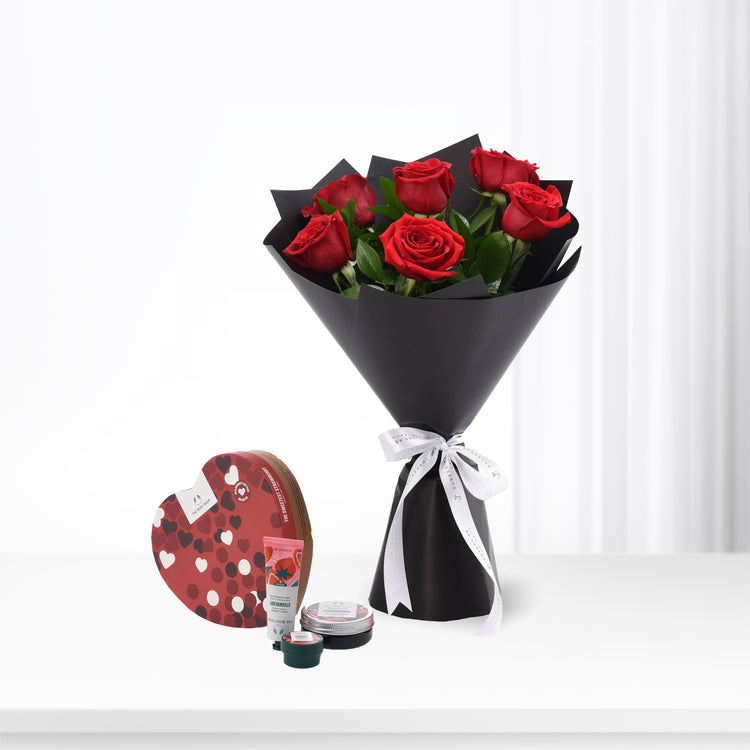 Vibrant red roses in black paper, white bow, paired with heart-shaped strawberry body care set.