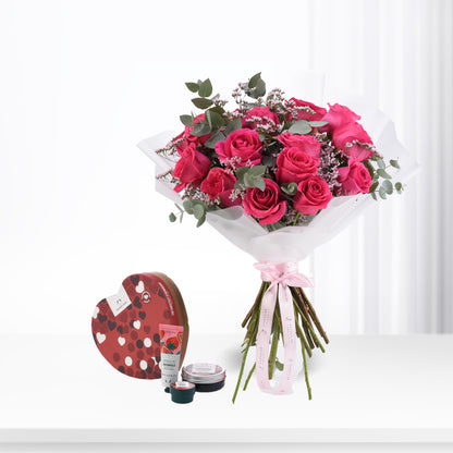 Vibrant pink roses with eucalyptus, wrapped in white paper and pink ribbon, paired with a heart-shaped The Body Shop gift set.