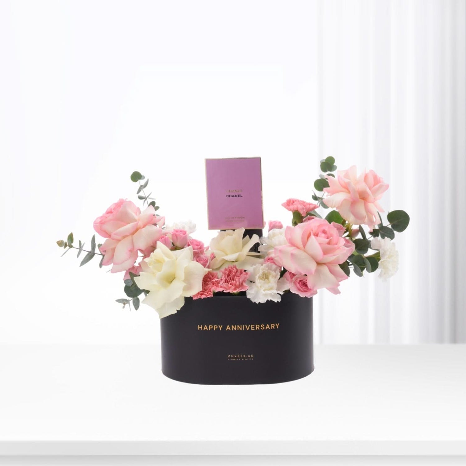 Elegant black anniversary box with pink roses, white blooms, and Chanel perfume.