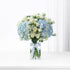 Elegant blue hydrangeas and white roses in clear vase with branded ribbon.